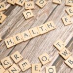 Scrabble tiles spelling 'HEALTH' on wooden surface, symbolizing wellness.